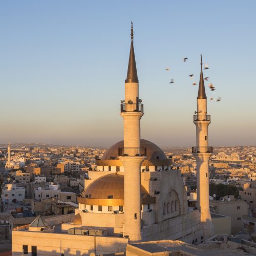 Cityscape at sunset, with mosque and minarets in the foreground.